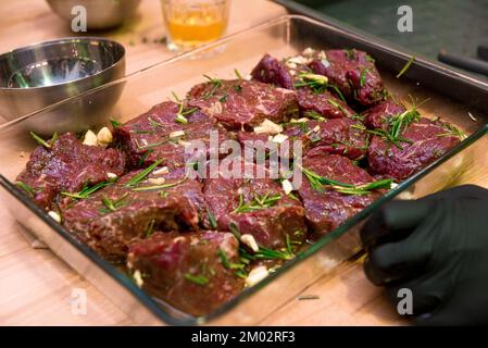 Gros morceaux de bœuf marinés dans l'huile, l'ail, le romarin et les épices dans un plat à pâtisserie en verre Banque D'Images