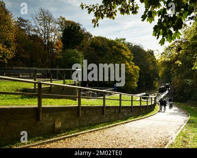 Personnes marchant sur le canal en automne par écluse, bateaux voyageant - Sunlit Bingley 5 Rise Locks, Leeds Liverpool Canal, West Yorkshire Angleterre Royaume-Uni. Banque D'Images