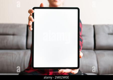 Person tenant une tablette numérique verticalement avec un écran blanc vierge face à l'appareil photo à la maison. Maquette de portrait pour applications mobiles et publicité. Banque D'Images