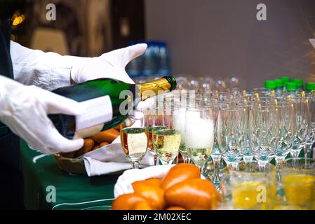 Le serveur verse du champagne dans des verres. Les mains du serveur sont en gants blancs. Banque D'Images