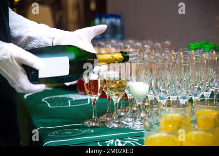 Le serveur verse du champagne dans des verres. Les mains du serveur sont en gants blancs. Banque D'Images