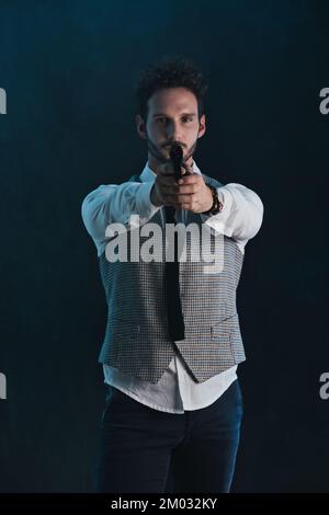 Beau homme en studio pointant le pistolet, sur fond sombre Banque D'Images