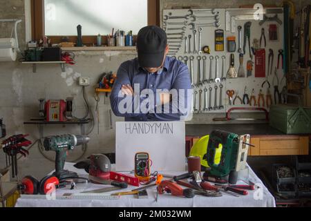 Image d'un homme souriant dans son atelier avec un banc plein d'outils de travail et le mot handyman. Homme capable de réparer et de réparer tout dans le ho Banque D'Images