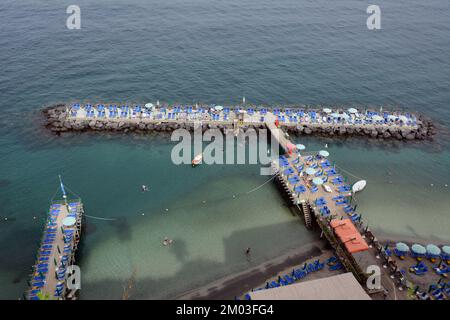 Une terrasse privée de club de plage avec chaise, parasols et nageurs, dans la mer Méditerranée, sous les falaises de Sorrento, Campanie, Italie. Banque D'Images