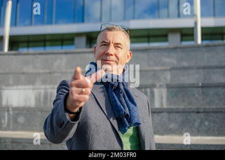 Portrait d'un homme d'âge moyen debout près des escaliers en béton d'un bâtiment moderne, pointant l'index vers la caméra en ville. Banque D'Images