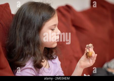 La jeune fille expressive mange du poulet et des légumes pour le dîner sur le canapé tout en regardant la télévision Banque D'Images