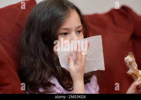 La jeune fille expressive mange du poulet et des légumes pour le dîner sur le canapé tout en regardant la télévision Banque D'Images