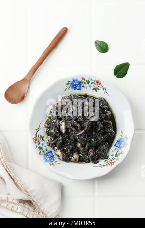 Tumis Cumi Hitam ou Squid frits Stir dans la sauce à l'encre noire. Cuisine indonésienne traditionnelle à base de calamar et de Spicy Seasoning sur White plate. Vue de dessus Banque D'Images