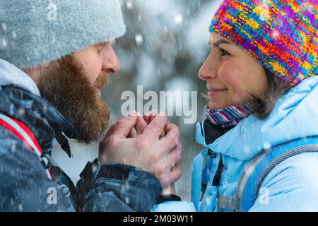 Couple de randonneurs d'âge moyen dans la forêt d'hiver. L'homme réchauffe les mains de la femme avec son souffle. Gros plan. Banque D'Images