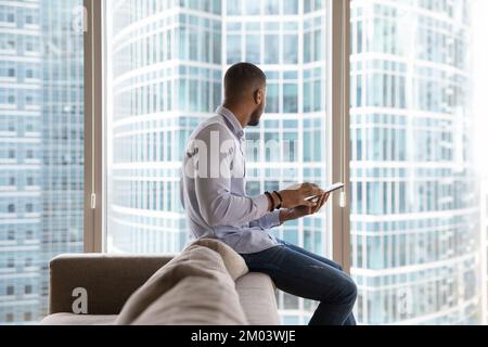 Jeune homme d'affaires africain tenant un ordinateur tablette, s'appuyant sur un canapé Banque D'Images