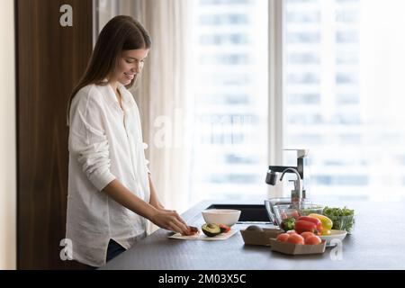 Positif joli cuisinier blogger fille préparant la salade dans la cuisine maison Banque D'Images