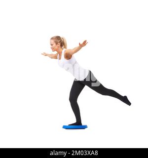 Parfaitement en harmonie avec son corps. Plein studio de prise de vue d'une jeune femme faisant des exercices d'équilibre isolé sur blanc. Banque D'Images