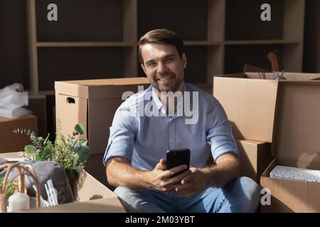 Heureux beau propriétaire millénaire homme à la maison utilisant le téléphone mobile Banque D'Images