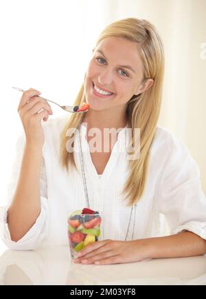 Commencez la journée par un petit déjeuner sain. Portrait d'une jeune femme attrayante mangeant de la salade de fruits pour le petit déjeuner. Banque D'Images