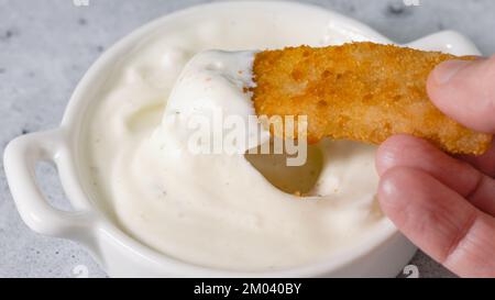 Croquant bâton de poisson pané fait de goberge d'Alaska pêché sauvage trempée dans du yaourt grec sauce à l'ail en gros plan sur la table de cuisine Banque D'Images