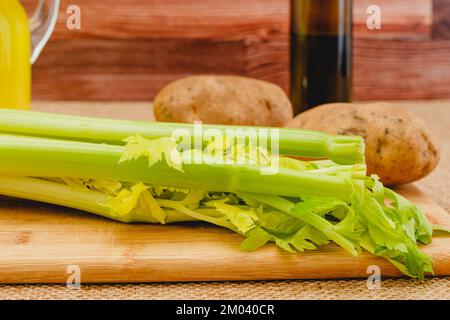 Branche de céleri et pommes de terre en gros plan sur panneau de bois. Légumes crus et huile d'olive. Ingrédients pour une recette de soupe de céleri Banque D'Images