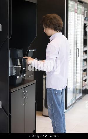 Un jeune homme prépare le café à l'aide d'un distributeur automatique professionnel Banque D'Images