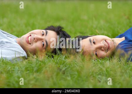 Partager les mêmes pensées et les mêmes rêves. Mignon jeune couple asiatique gay souriant ensemble tout en étant allongé sur l'herbe. Banque D'Images