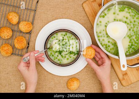Soupe crémeuse de céleri aux petits pois verts. Femme mangeant de la soupe de légumes frais cuits, servie avec du pain au fromage frais, plat Banque D'Images