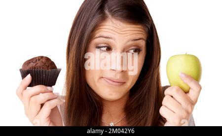 J'ai fait mon choix. Une jeune femme attrayante qui décide entre une pomme et un muffin. Banque D'Images