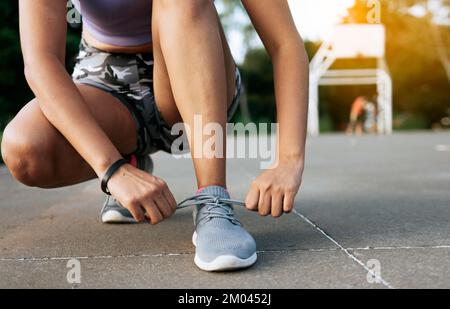 Une fille sportive enfile ses lacets de chaussures dans un parc. Une fille de coureur a noué ses chaussures de course dans un parc avec un espace pour le texte, gros plan d'une femme sportive portant ses chaussures Banque D'Images