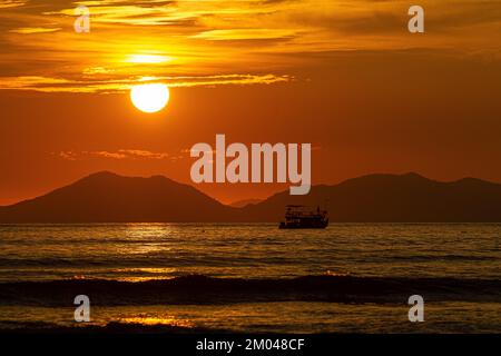 En bateau à la mer, les vagues éclatent contre le ciel doré et le soleil brille magnifiquement dans le ciel entouré de montagnes. Banque D'Images