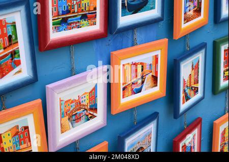 D'en haut des cadres multicolores avec des images lumineuses de canaux accrochés au mur bleu sur la rue de l'île de Burano Banque D'Images