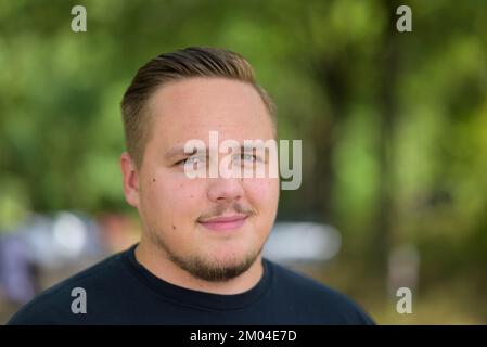 Jeune homme souriant à la caméra dans un amusement dans un gros plan tête dans un jardin Banque D'Images