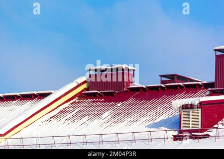 Toit rouge d'une maison dans la neige. Symbole des fêtes du nouvel an, Noël et l'arrivée du Père Noël. La neige coule sur le toit avec une cheminée. Banque D'Images