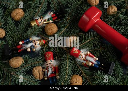 Haltères de gym, figurines de Noël et noix de Grenoble sur les branches des arbres. Saison des fêtes de remise en forme, composition d'entraînement d'hiver. Banque D'Images