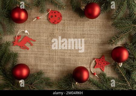 Décorations de Noël en boules, décorations suspendues et branches d'arbre vertes. Composition de la couche plate d'hiver de la saison des fêtes avec espace de copie sur le tissu de jute. Banque D'Images