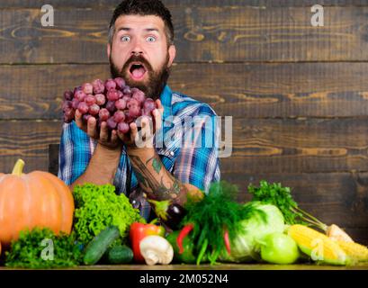 Récolte de chez nous avec l'agriculteur sur la table. Farmer fiers de récolter les légumes et les raisins. L'homme détient fond de bois barbu raisins. Bio Légumes Banque D'Images