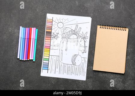 Page de coloriage, feutres et bloc-notes sur fond sombre Banque D'Images