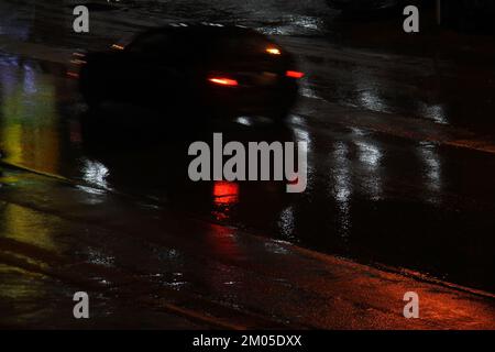 Une voiture floue qui s'emballe avec des sentiers de queue lors d'une nuit de pluie. Banque D'Images