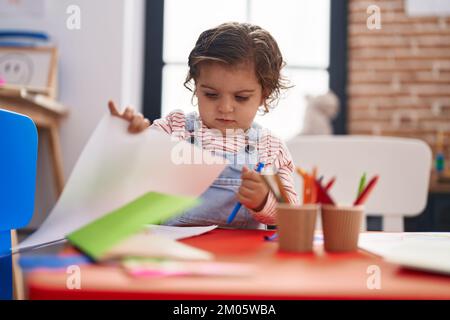 Adorable étudiante hispanique de fille assise sur table de dessin sur papier à la maternelle Banque D'Images