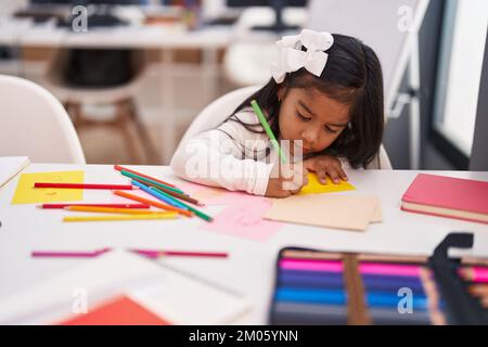 Adorable étudiante hispanique de fille assise sur le dessin de table sur le papier en classe Banque D'Images