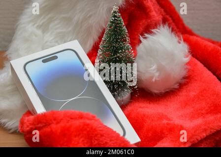 Riga, Lettonie - 4 décembre 2022: Apple iPhone 14 pro smartphone cadeau de Noël sur un chapeau de Père Noël rouge à côté d'un petit vert artificiel de Noël tre Banque D'Images