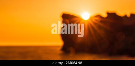 Bannière. Dans le flou un coucher de soleil épique sur la mer - le soleil se couche derrière la montagne et tout brille avec la lumière chaude avec de longs rayons. Banque D'Images