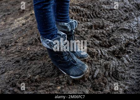 Les pieds de l'enfant dans des bottes sales colorées, sur fond boueux. Sale dans la boue bottes chaudes. Photo de haute qualité Banque D'Images
