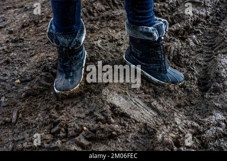 Les pieds de l'enfant dans des bottes sales colorées, sur fond boueux. Sale dans la boue bottes chaudes. Photo de haute qualité Banque D'Images