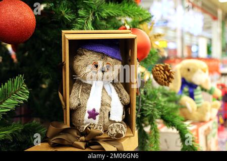 Chat jouet dans une boîte cadeau et arbre de Noël sur fond de lumières floues. Souvenirs de fête dans un magasin, symbole du nouvel an chinois 2023 Banque D'Images