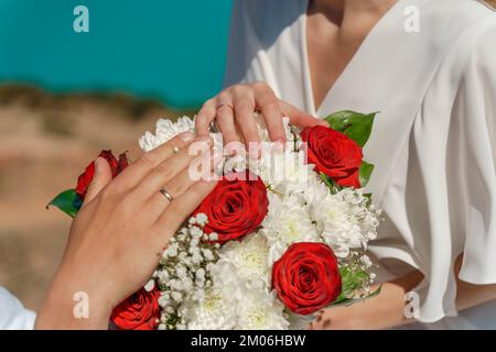 Mains du marié et de la mariée avec des anneaux de mariage sur le bouquet de la mariée Banque D'Images