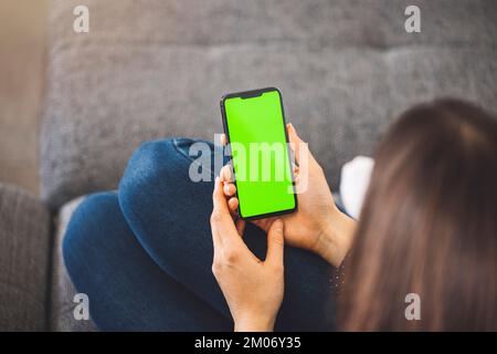 Sur le coup de tête d'une femme méconnaissable assise sur le canapé avec un téléphone dans les mains. Écran vert du téléphone Banque D'Images