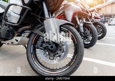 Gros plan vue détaillée roue avant de moto moderne roue avant de l'aile en fibre de carbone disque de frein de fourche garée dans la rue de la ville. Beaucoup de motos sur le parking de la ville Banque D'Images