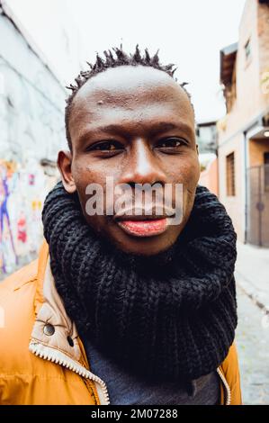 portrait vertical en gros plan du jeune africain, portant un foulard, debout dans la rue, sérieux et regardant l'appareil photo. Banque D'Images