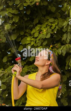 Jardin d'été, arrosage - belle fille arrosoir roses avec tuyau de jardin dans le jardin Banque D'Images