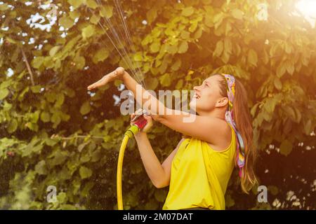 jeune jolie fille s'amusant dans le jardin arroser des plantes avec un tuyau. Souriant tout en prenant un passe-temps préféré Banque D'Images