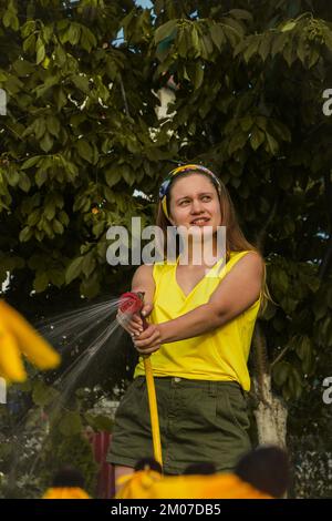 jeune jolie fille s'amusant dans le jardin arroser des plantes avec un tuyau. Souriant tout en prenant un passe-temps préféré Banque D'Images