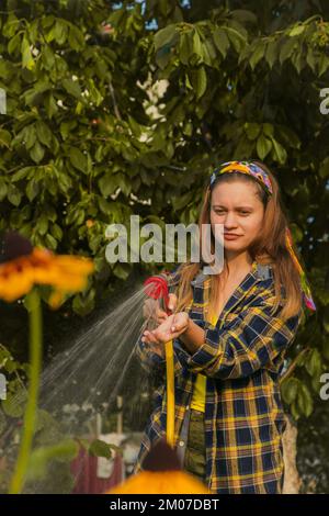 jeune jolie fille s'amusant dans le jardin arroser des plantes avec un tuyau. Souriant tout en prenant un passe-temps préféré Banque D'Images