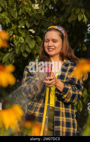 jeune jolie fille s'amusant dans le jardin arroser des plantes avec un tuyau. Souriant tout en prenant un passe-temps préféré Banque D'Images